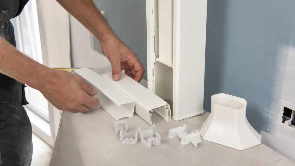 close-up of an installer sorting a GTL trunking body, partial covers, adjustable cable clips and a floor junction flare before wall mounting, no text or logos