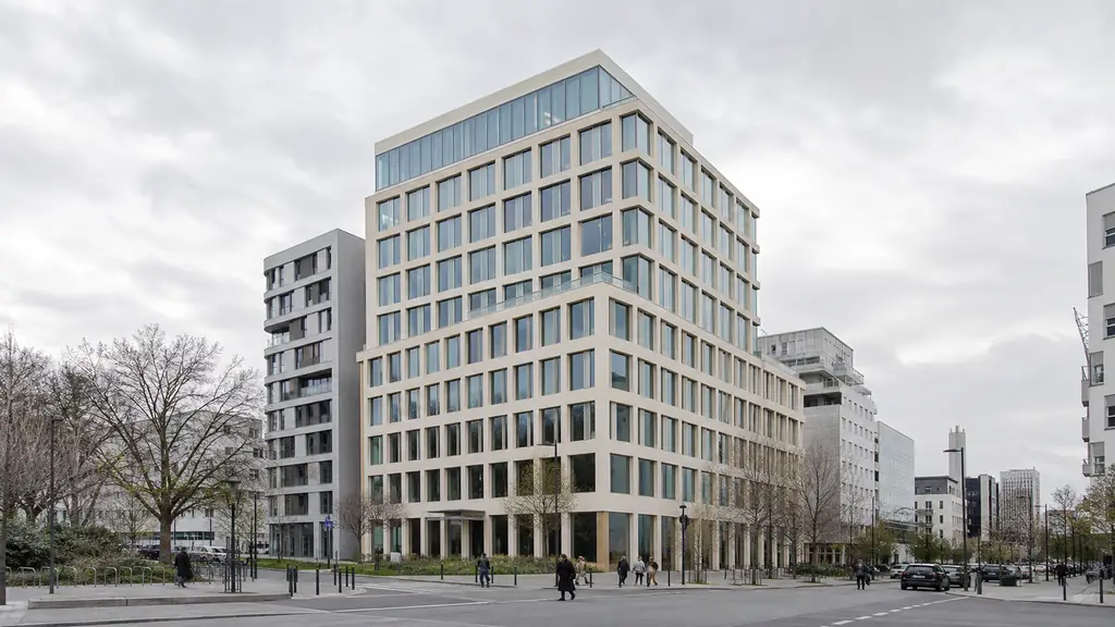 Editorial street-level photograph of the contemporary nine-storey Arc de Seine office building at avenue Pierre-Mendès-France and rue Paul-Klee in Paris 13th, showing its urban scale within the Paris Rive Gauche district, no text or logos